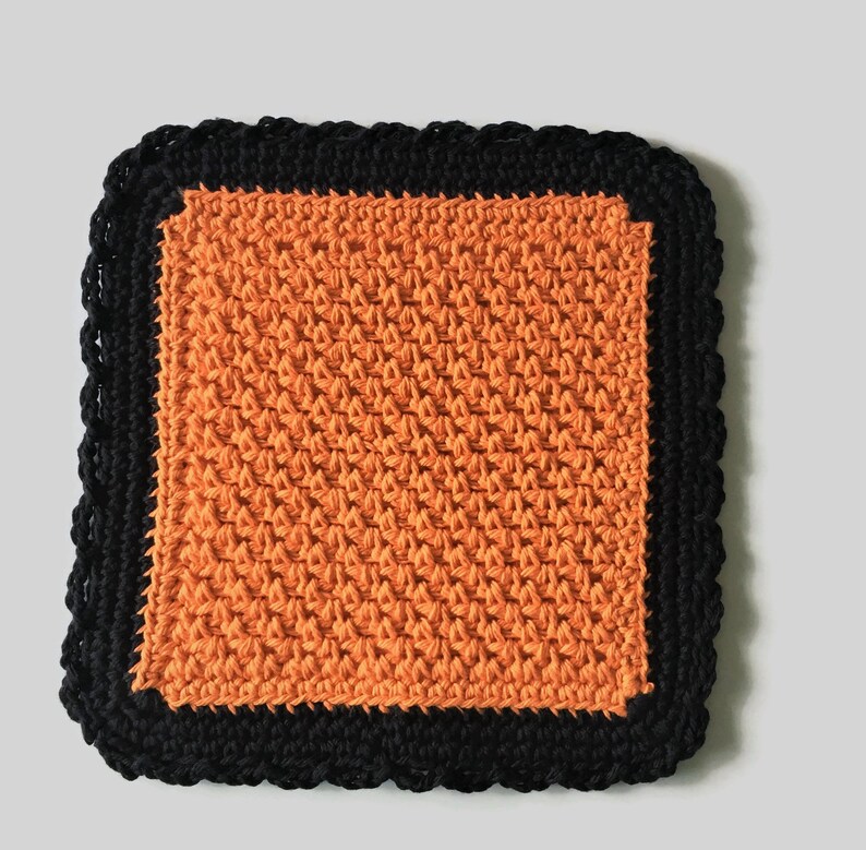 May include: Orange crochet dishcloth with a black crocheted border.
