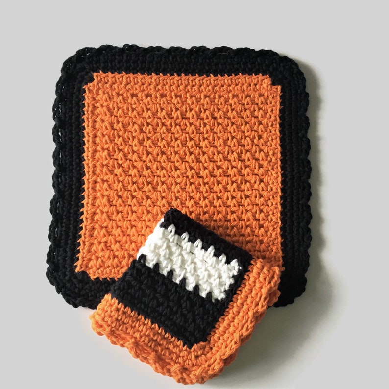 May include: Two crocheted dishcloths, one orange with a black border and one orange, black, and white.