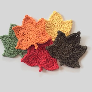 May include: Five crocheted maple leaf coasters in different colors: green, orange, red, brown, and yellow.