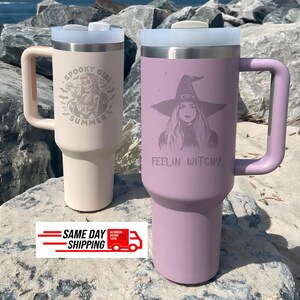 May include: Two stainless steel tumblers with handles and translucent lids. The beige tumbler features a skeleton graphic with the text SPOOKY GIRL SUMMER. The lavender tumbler features a witch graphic with the text FEELIN' WITCHY.