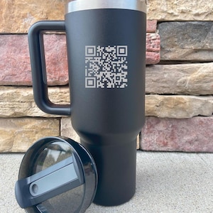 May include: Black stainless steel travel mug with a black lid and a handle. The mug has a QR code engraved on the side.