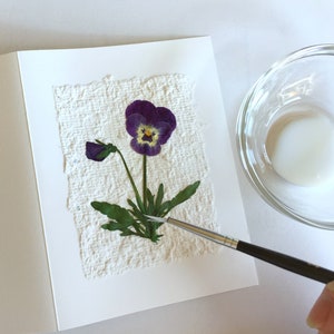 Adding pressed violets to a notecard with recycled paper.