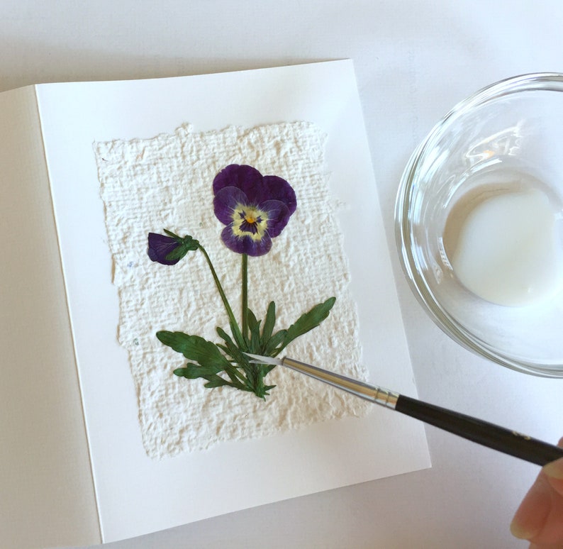 Adding pressed violets to a notecard with recycled paper.