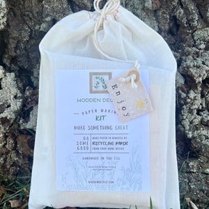 K&ouml;nnte beinhalten: Ein wei&szlig;er Baumwollbeutel mit Kordelzug, einem Etikett mit der Aufschrift "Enjoy" und einem bedruckten Etikett mit der Aufschrift "Wooden Deckle - Paper Making Kit - Make Something Great - Do Some Good - Make paper in minutes by recycling paper from your home office - Handmade in the USA - woodendeckle.com".