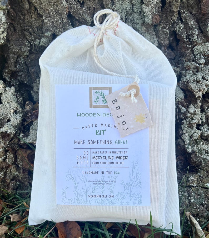 K&ouml;nnte beinhalten: Ein wei&szlig;er Baumwollbeutel mit Kordelzug, einem Etikett mit der Aufschrift "Enjoy" und einem bedruckten Etikett mit der Aufschrift "Wooden Deckle - Paper Making Kit - Make Something Great - Do Some Good - Make paper in minutes by recycling paper from your home office - Handmade in the USA - woodendeckle.com".