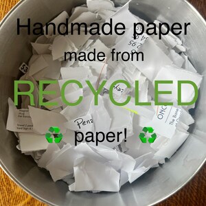K&ouml;nnte beinhalten: Eine silberne Sch&uuml;ssel gef&uuml;llt mit zerkleinertem wei&szlig;em Papier. Das Papier ist mit den Worten "Handgemachtes Papier aus recyceltem Papier!" beschriftet.