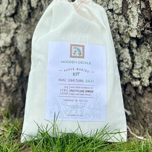 K&ouml;nnte beinhalten: Ein wei&szlig;er Stoffbeutel mit einem Etikett, auf dem steht "Wooden Deckle Paper Making Kit Make Something Great Do Some Good Recycling Paper from your home office Handmade in the USA WoodenDeckle.com".