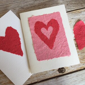 K&ouml;nnte beinhalten: Zwei handgemachte Karten mit roten Papierherzen auf wei&szlig;em Karton. Die Herzen sind aus strukturiertem Papier.
