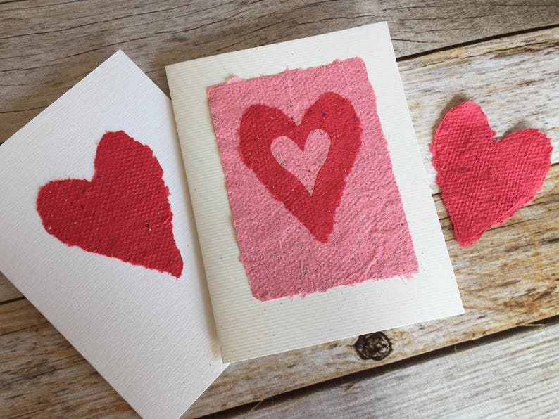 K&ouml;nnte beinhalten: Zwei handgemachte Karten mit roten Papierherzen auf wei&szlig;em Karton. Die Herzen sind aus strukturiertem Papier.