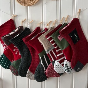 May include: A collection of Christmas stockings in various colors and patterns, including red, green, and gray, are hung from a string with wooden clothespins. Woven baskets and circular wall decor are visible in the background.