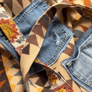 May include: A patchwork tote bag with denim pockets and a patterned fabric design. The bag features a geometric pattern in shades of brown, tan, and yellow, with floral accents on the straps. The denim pockets add a touch of casual style.