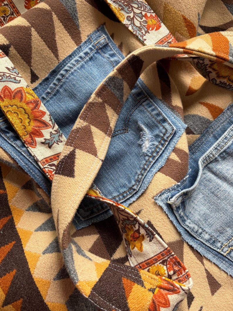 May include: A patchwork tote bag with denim pockets and a patterned fabric design. The bag features a geometric pattern in shades of brown, tan, and yellow, with floral accents on the straps. The denim pockets add a touch of casual style.