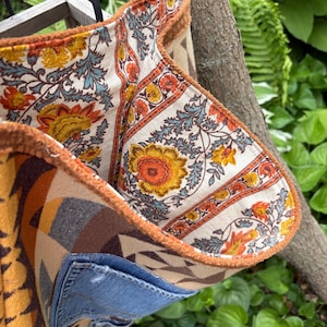 May include: A handmade tote bag with a patchwork design. The bag features a denim pocket and is lined with a floral patterned fabric in orange, yellow, and blue. The exterior has a geometric pattern in shades of brown and tan.
