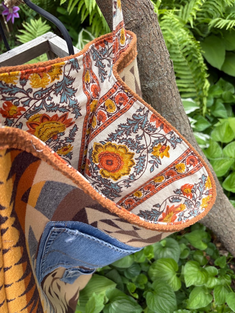 May include: A handmade tote bag with a patchwork design. The bag features a denim pocket and is lined with a floral patterned fabric in orange, yellow, and blue. The exterior has a geometric pattern in shades of brown and tan.