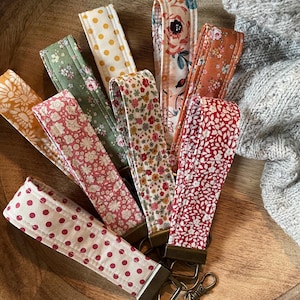 May include: A set of eight fabric keychains with different patterns, including floral, polka dot, and geometric designs. The keychains are attached to a silver key ring.