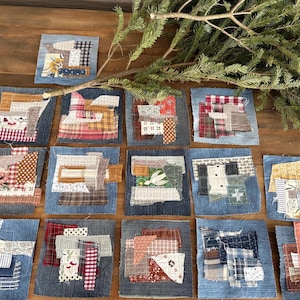 May include: A collection of small, square fabric art pieces. Each piece is a patchwork of various fabrics, including denim, floral prints, and plaid. The color palette includes blues, reds, browns, and creams. A sprig of evergreen branches is in the background.