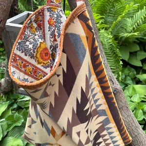 May include: A reversible tote bag with a floral pattern on one side and a geometric pattern on the other. The floral side features orange, yellow, and blue flowers on a cream background. The geometric side has a beige, brown, and gray design.