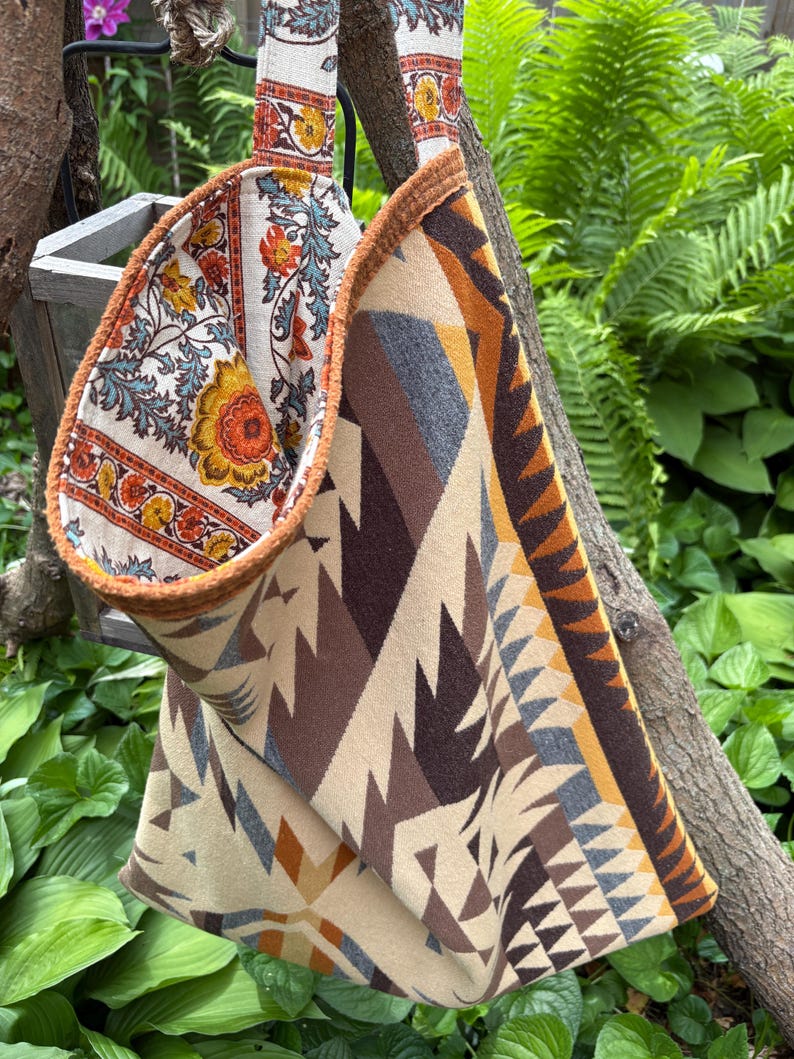 May include: A reversible tote bag with a floral pattern on one side and a geometric pattern on the other. The floral side features orange, yellow, and blue flowers on a cream background. The geometric side has a beige, brown, and gray design.
