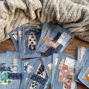 May include: A collection of rectangular denim fabric patches featuring various layered textile scraps in shades of blue, white, brown, and yellow. Each patch displays a unique combination of floral, geometric, and solid patterns with visible stitching.