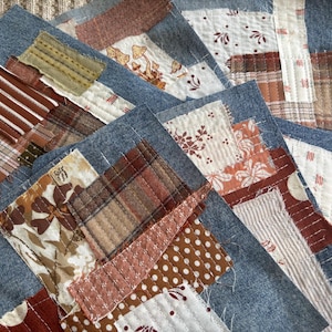 May include: A collection of fabric squares featuring blue denim bases layered with various textile patches. The patches include brown and white stripes, plaid patterns, floral prints, polka dots, and mushroom illustrations, all secured with visible white stitching.