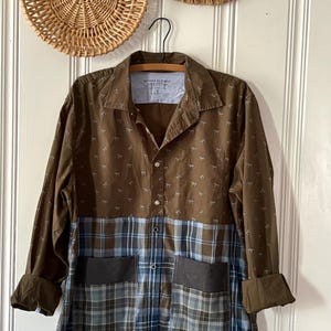 May include: A long-sleeve button-down shirt featuring a brown upper section with a small repeating horse pattern and a blue and brown plaid lower section. The shirt includes two front pockets and a label reading Banana Republic Luxe Poplin.