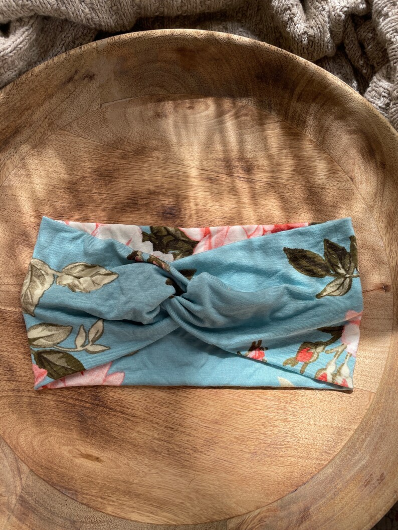 May include: A blue headband with a floral pattern. The headband is twisted and has a knot in the center.