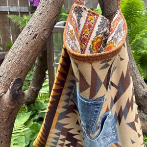 May include: A handmade tote bag with a geometric pattern in shades of brown, tan, and yellow. The bag features two denim pockets and a floral patterned lining. The straps and trim have a floral design.