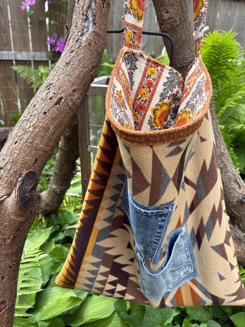 May include: A handmade tote bag with a geometric pattern in shades of brown, tan, and yellow. The bag features two denim pockets and a floral patterned lining. The straps and trim have a floral design.