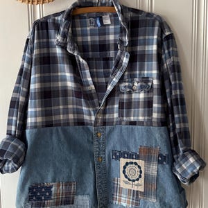 May include: A long-sleeve button-down shirt featuring a blue and white plaid pattern on the upper portion and a solid light blue denim lower section. The denim area includes various fabric patches, including one with a stitched flower design.