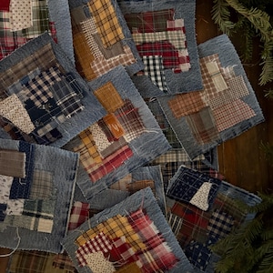 May include: A collection of square fabric patches with a denim border. Each patch features a unique patchwork design with various patterns and colors, including red, yellow, blue, and white. The patches are arranged on a wooden surface, with some greenery in the background.