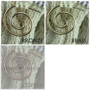 May include: Three metal knitting stitch markers in the shapes of a spiral. The markers are shown on a white knitted fabric. The markers are bronze, brass, and copper.