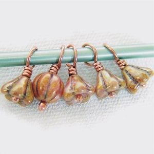 May include: Six copper stitch markers with a bell-shaped, cream-colored ceramic bead with brown and pink marbling.