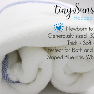 May include: A white hooded towel with blue and white striped trim. The towel is rolled up and is labeled "tiny Sunshine Hooded Towels". The text also says "Newborn to Age 3", "Generously-sized 33 x 33", "Thick + Soft + Cozy", "Perfect for Bath and Beach", and "Striped Blue and White Trim".