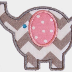 May include: An embroidered elephant applique with a gray and white chevron pattern body. The elephant has a pink ear with white polka dots and a blue eye. The applique is outlined with gray stitching.
