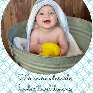 May include: A baby wearing a white hooded towel with blue trim sits in a metal tub. The baby is holding a yellow rubber ducky. The towel has the word "Cha" embroidered on it.