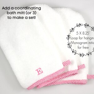 May include: White bath mitts with pink striped trim and a loop for hanging. Each mitt is embroidered with a pink initial. The mitts measure 5 x 8.25 inches.