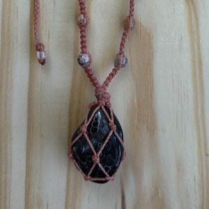 Pink necklace with neutral beads lining all the way up the neckline with 5 knots between each bead. The Agate is caged in the necklace and it is a dark black/deep green with fossilized snails that are in the front of the stone.