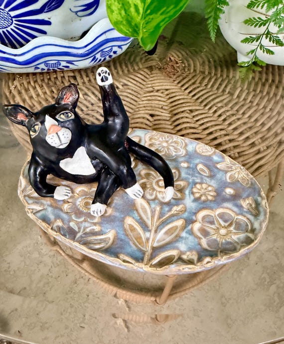 A one-of-a-kind hand-thrown ceramic cat dish where the tuxedo cat IS the ring holder — functional pottery meets quirky sculptural art.