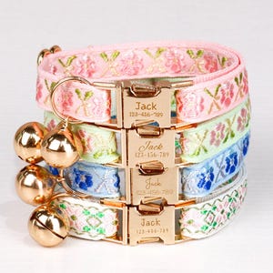 May include: Stacked collection of embroidered cat collars in pink, green, blue, and white. Each collar features a gold-colored buckle engraved with the name "Jack" and a phone number. Gold bell charms hang from the top collar.