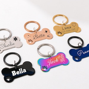 May include: Various bone-shaped pet tags in different colours, including silver, rose gold, gold, black, blue, and iridescent. Each tag is engraved with a name, and some feature paw prints and floral patterns.