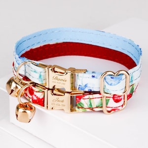 Può includere: Due collari personalizzati per gatti. Uno è azzurro e rosso, l'altro è rosso con un motivo floreale. Entrambi hanno fibbie e campanelli color oro. I collari sono incisi con i nomi "Davis" e "Jack" e numeri di telefono.