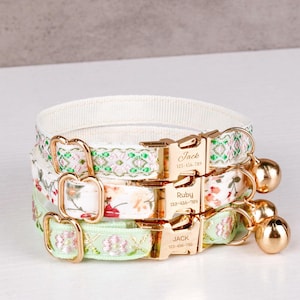 May include: Three personalized cat collars with gold-colored buckles and bells. The collars feature floral and patterned designs in white, pink, and green. Each buckle is engraved with a name and phone number.