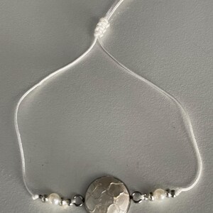 May include: White string bracelet with a white and silver round charm and two white pearl beads.