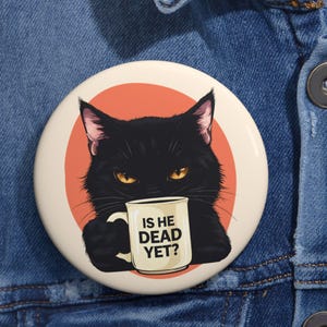 May include: Round button with a black cat illustration holding a mug. The cat has yellow eyes and is set against an orange circle. The mug reads "IS HE DEAD YET?"