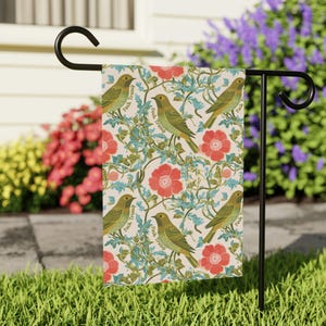 May include: A garden flag featuring a repeating pattern of olive green birds, red flowers, and teal vines on a cream background. The text "Fuck Trump" is printed on the flag. The flag is displayed on a black metal stand.