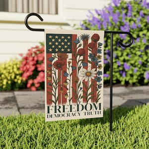 May include: A garden flag featuring a floral design with an American flag motif. The flag has red and white stripes with a green corner of stars and a variety of flowers. The words "FREEDOM DEMOCRACY TRUTH" are printed at the bottom.