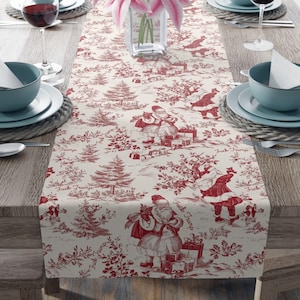 May include: A cream-colored Christmas table runner with a red toile pattern featuring Santa Claus figures, Christmas trees, and the text "Fuck Trump". The runner is set on a wooden table, with place settings visible.