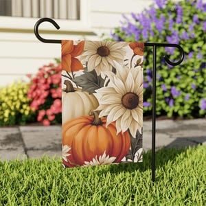 May include: A garden flag featuring a fall harvest design. The flag displays a vibrant arrangement of pumpkins, sunflowers, and other autumn flowers in shades of orange, cream, and brown. The flag is displayed on a black metal stand, perfect for outdoor decor.