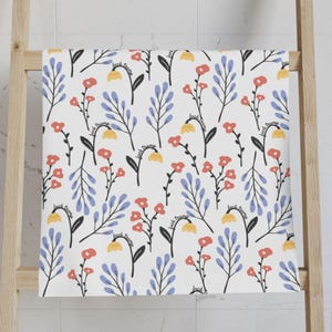 May include: White bath towel with a floral pattern featuring red and yellow flowers, blue leaves, and the text "fuck trump" in black. The towel is hanging on a wooden ladder.
