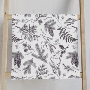 May include: White bath towel with a black botanical pattern of pinecones, ferns, and sprigs. The words "Fuck Trump" are repeated throughout the design. The towel is draped over a wooden ladder.